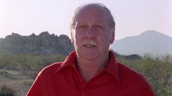 Movie still from “The Hills Have Eyes” (1977), directed by Wes Craven – An older man wearing a red shirt in front of mountains; Close Up shot, Low angle
