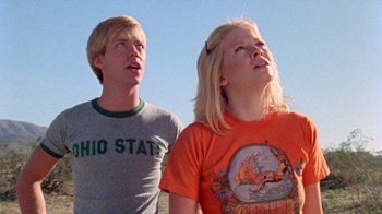 Movie still from “The Hills Have Eyes” (1977), directed by Wes Craven – A man and a woman standing next to each other looking up; Medium shot, Low angle