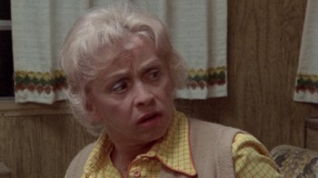 Movie still from “The Hills Have Eyes” (1977), directed by Wes Craven – An older woman in a yellow shirt is looking at the camera; Close Up shot, Over the shoulder angle