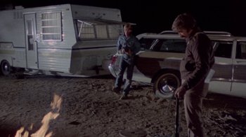Movie still from “The Hills Have Eyes” (1977), directed by Wes Craven – Two people standing next to a car and a trailer; Wide shot, High angle