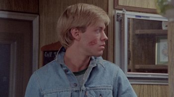 Movie still from “The Hills Have Eyes” (1977), directed by Wes Craven – A young man wearing a jean jacket with a patch on his face; Close Up shot, Over the shoulder angle
