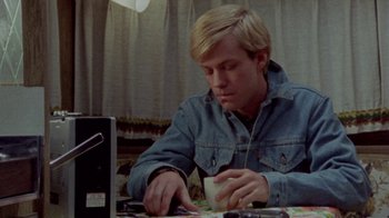 Movie still from “The Hills Have Eyes” (1977), directed by Wes Craven – A man sitting in front of a computer desk; Medium shot, High angle