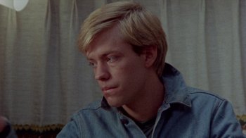 Movie still from “The Hills Have Eyes” (1977), directed by Wes Craven – A man with blonde hair sitting in front of a curtain; Close Up shot, High angle
