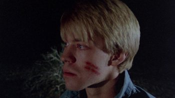 Movie still from “The Hills Have Eyes” (1977), directed by Wes Craven – A young man with red marks on his face; Close Up shot, High angle