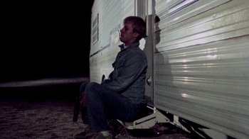Movie still from “The Hills Have Eyes” (1977), directed by Wes Craven – A man sitting on the side of a trailer at night; Wide shot, Low angle
