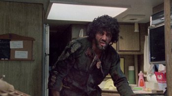 Movie still from “The Hills Have Eyes” (1977), directed by Wes Craven – A man with a beard is standing in a kitchen; Medium shot, Low angle