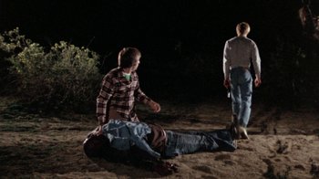 Movie still from “The Hills Have Eyes” (1977), directed by Wes Craven – Two men standing over a dead body in the dirt; Wide shot, High angle