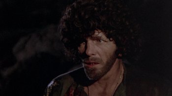 Movie still from “The Hills Have Eyes” (1977), directed by Wes Craven – A person with a beard and curly hair; Close Up shot, Over the shoulder angle
