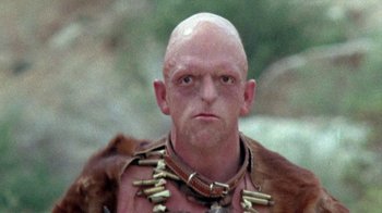 Movie still from “The Hills Have Eyes” (1977), directed by Wes Craven – A bald man wearing a necklace and a fur coat; Close Up shot, Low angle