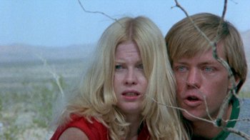 Movie still from “The Hills Have Eyes” (1977), directed by Wes Craven – A woman and a man standing next to each other in a field; Close Up shot, Low angle