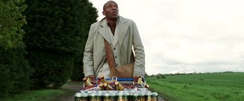 Movie still from “The Hitchhiker's Guide to the Galaxy” (2005), directed by Garth Jennings – A man standing next to a table full of cans of beer; Medium shot, Low angle