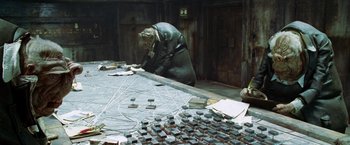 Movie still from “The Hitchhiker's Guide to the Galaxy” (2005), directed by Garth Jennings – A man in a trench coat is working on a table; Wide shot, High angle
