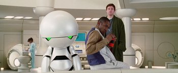 Movie still from “The Hitchhiker's Guide to the Galaxy” (2005), directed by Garth Jennings – Two men standing in front of a silver robot; Medium shot, Over the shoulder angle