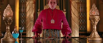 Movie still from “The Hitchhiker's Guide to the Galaxy” (2005), directed by Garth Jennings – A man in a red shirt and a gold chain around his neck; Medium shot, Low angle