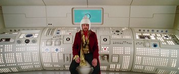 Movie still from “The Hitchhiker's Guide to the Galaxy” (2005), directed by Garth Jennings – A man sitting on top of a toilet in a room; Wide shot, Low angle