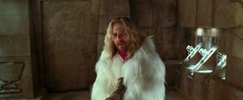Movie still from “The Hitchhiker's Guide to the Galaxy” (2005), directed by Garth Jennings – A man with long blonde hair and a white fur coat; Medium shot, Over the shoulder angle