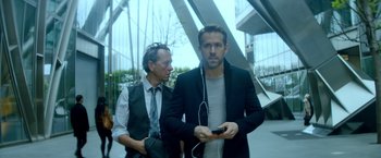 Movie still from “The Hitman's Bodyguard” (2017), directed by Patrick Hughes – A man in a suit and tie holding a cell phone; Medium shot, Over the shoulder angle