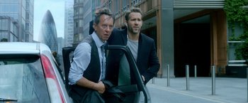 Movie still from “The Hitman's Bodyguard” (2017), directed by Patrick Hughes – A couple of men standing next to each other on a street; Medium shot, Over the shoulder angle