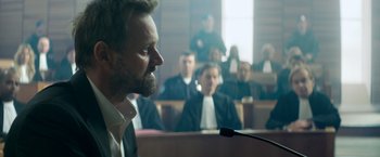 Movie still from “The Hitman's Bodyguard” (2017), directed by Patrick Hughes – A man is speaking in front of a group of people; Medium shot, Over the shoulder angle