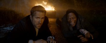 Movie still from “The Hitman's Bodyguard” (2017), directed by Patrick Hughes – Two men laying on the ground in front of a burning car; Medium shot, High angle