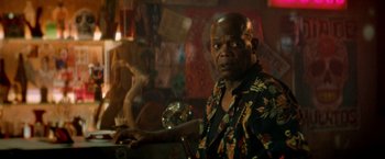 Movie still from “The Hitman's Bodyguard” (2017), directed by Patrick Hughes – An older man in a colorful shirt is looking at the camera; Medium shot, Over the shoulder angle