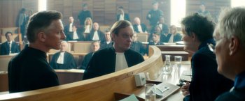 Movie still from “The Hitman's Bodyguard” (2017), directed by Patrick Hughes – A man sitting in front of a crowd in a courtroom; Medium shot, Over the shoulder angle