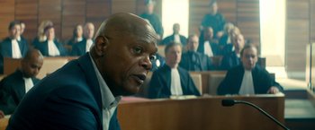Movie still from “The Hitman's Bodyguard” (2017), directed by Patrick Hughes – A man sitting in front of a group of people; Medium shot, Over the shoulder angle