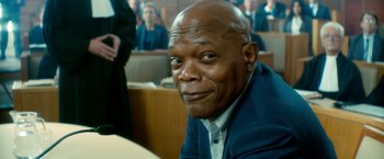 Movie still from “The Hitman's Bodyguard” (2017), directed by Patrick Hughes – A man in a suit sitting in front of a group of people in a court room; Close Up shot, Low angle