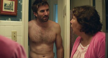 Movie still from “The Hollars” (2016), directed by John Krasinski – A shirtless man and a woman looking in a mirror; Medium shot, Over the shoulder angle
