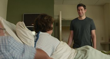 Movie still from “The Hollars” (2016), directed by John Krasinski – A man standing in front of a woman in a hospital bed; Medium shot, Over the shoulder angle