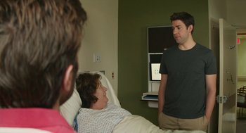 Movie still from “The Hollars” (2016), directed by John Krasinski – A man standing next to a woman in a hospital bed; Medium shot, Over the shoulder angle