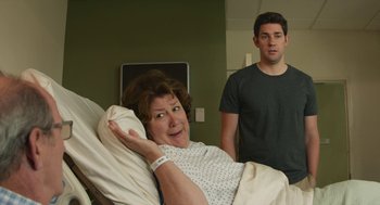 Movie still from “The Hollars” (2016), directed by John Krasinski – A man standing next to a woman in a hospital bed; Medium shot, Over the shoulder angle