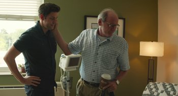 Movie still from “The Hollars” (2016), directed by John Krasinski – A man standing next to another man holding a cup; Medium shot, Over the shoulder angle