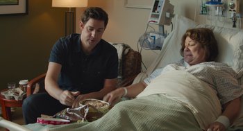 Movie still from “The Hollars” (2016), directed by John Krasinski – A man sitting next to a woman in a hospital bed; Medium shot, Over the shoulder angle