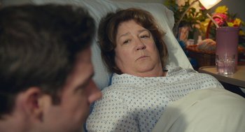 Movie still from “The Hollars” (2016), directed by John Krasinski – An older woman laying in a hospital bed; Close Up shot, Over the shoulder angle