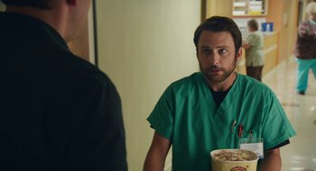 Movie still from “The Hollars” (2016), directed by John Krasinski – A man in a green scrub suit looking at a man in a black shirt in front of a mirror; Medium shot, Over the shoulder angle