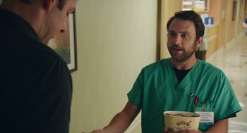 Movie still from “The Hollars” (2016), directed by John Krasinski – A man in a green scrub shirt shaking hands with another man in a green scrub suit; Medium shot, Over the shoulder angle
