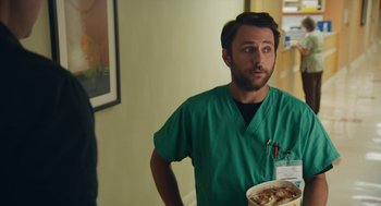 Movie still from “The Hollars” (2016), directed by John Krasinski – A man in a green shirt holding a plate of food; Medium shot, Over the shoulder angle
