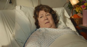 Movie still from “The Hollars” (2016), directed by John Krasinski – An older woman laying in a hospital bed; Close Up shot, Over the shoulder angle
