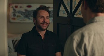 Movie still from “The Hollars” (2016), directed by John Krasinski – A man in a black shirt is smiling at the camera; Close Up shot, Over the shoulder angle