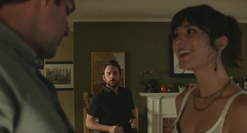 Movie still from “The Hollars” (2016), directed by John Krasinski – A man standing in a living room next to two other people; Medium shot, Over the shoulder angle