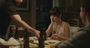 Movie still from “The Hollars” (2016), directed by John Krasinski – A woman sitting at a dinner table with a beer in her hand; Medium shot, Over the shoulder angle