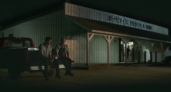 Movie still from “The Hollars” (2016), directed by John Krasinski – A couple of men sitting next to each other on top of a bench; Wide shot, Low angle