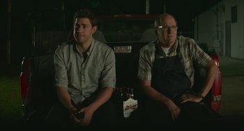 Movie still from “The Hollars” (2016), directed by John Krasinski – Two men sitting next to each other in a dark room; Medium shot, Low angle