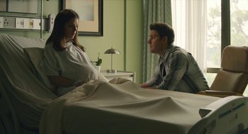 Movie still from “The Hollars” (2016), directed by John Krasinski – A man and a pregnant woman sitting in a hospital bed; Medium shot, Over the shoulder angle