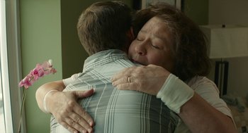 Movie still from “The Hollars” (2016), directed by John Krasinski – An older woman is hugging a younger man; Close Up shot, Over the shoulder angle