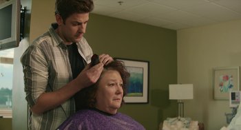 Movie still from “The Hollars” (2016), directed by John Krasinski – A man cutting a woman's hair in a room; Close Up shot, Over the shoulder angle