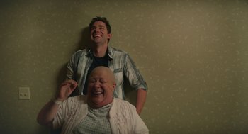 Movie still from “The Hollars” (2016), directed by John Krasinski – A man standing next to an older woman in front of a wall; Medium shot, Over the shoulder angle