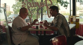 Movie still from “The Hollars” (2016), directed by John Krasinski – Two men sitting at a table in front of each other; Medium shot, Over the shoulder angle