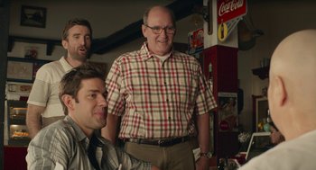 Movie still from “The Hollars” (2016), directed by John Krasinski – A man standing next to two other men in a room; Medium shot, Over the shoulder angle